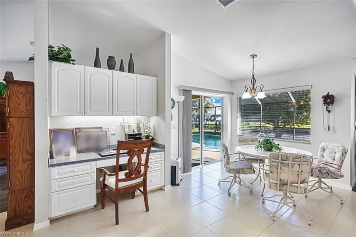 Dining room with built in desk, vaulted ceiling, light tile patterned floors, and a chandelier