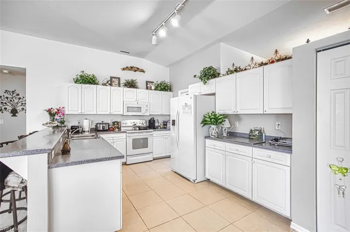 Kitchen with a breakfast bar area, white cabinetry, a peninsula, lofted ceiling, and white appliances