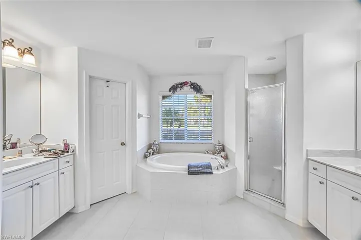 Bathroom featuring two vanities, a shower stall, a garden tub, and light tile patterned floors