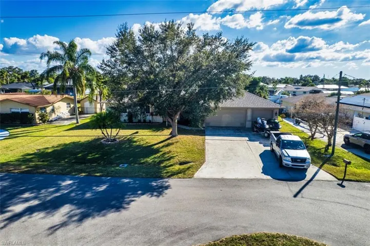 View of property hidden behind natural elements with driveway, a residential view, a front lawn, and a garage