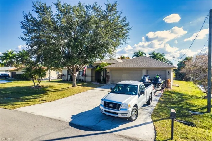 View of front of house with a front yard, a garage, driveway, and a shingled roof