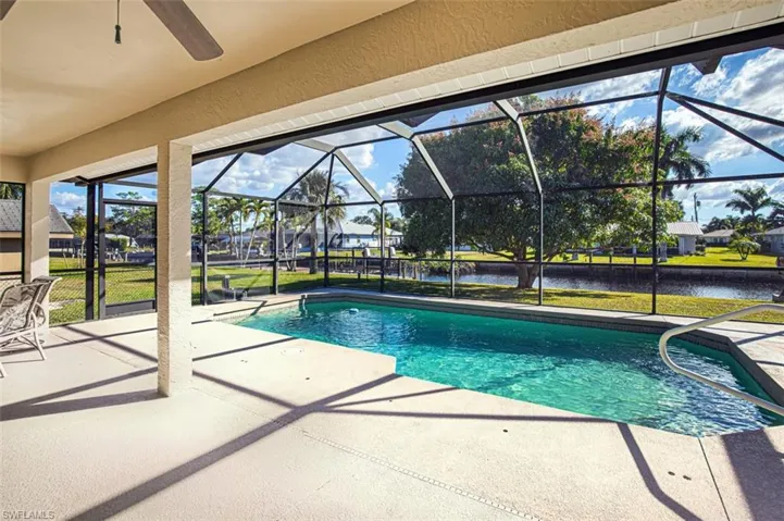 Outdoor pool featuring a patio area, a sunroom, a water view, glass enclosure, and a lawn