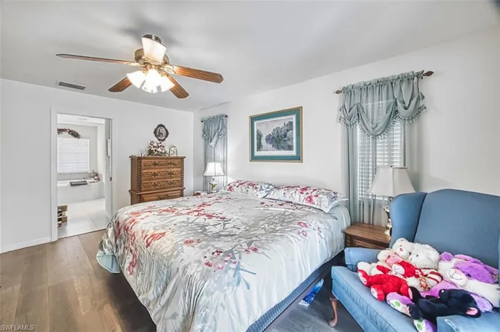 Bedroom with wood finished floors, a ceiling fan, ensuite bathroom, and multiple windows