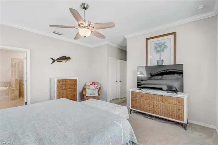 Carpeted bedroom featuring ornamental molding, ceiling fan, and ensuite bath