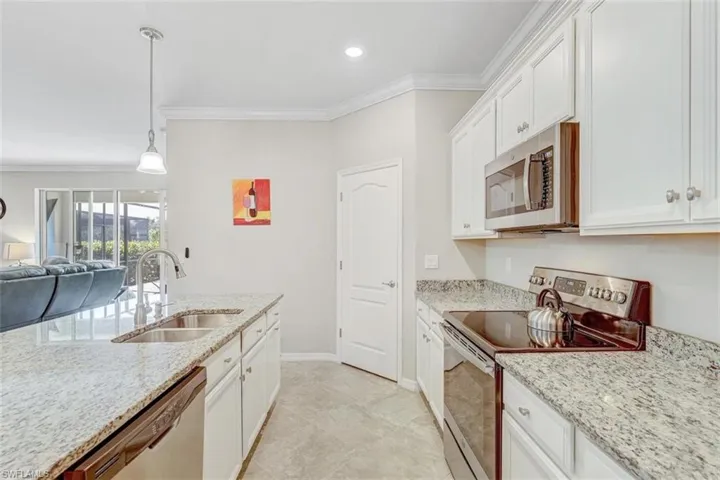 Kitchen with stainless steel appliances, white cabinetry, ornamental molding, open floor plan, and decorative light fixtures