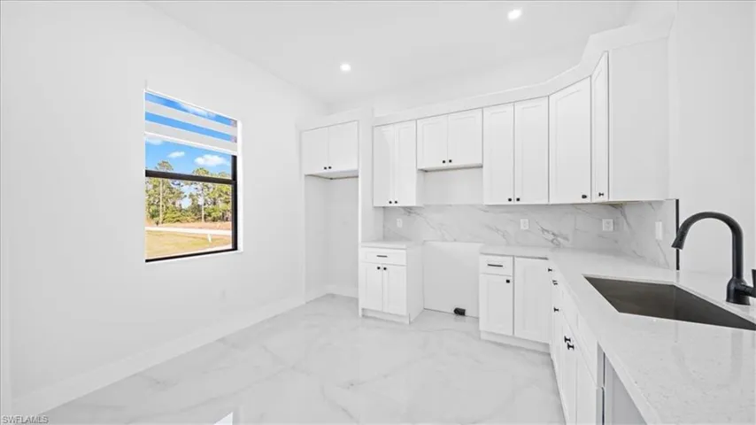 Kitchen featuring white cabinets, light stone countertops, decorative backsplash, light marble finish floors, and recessed lighting