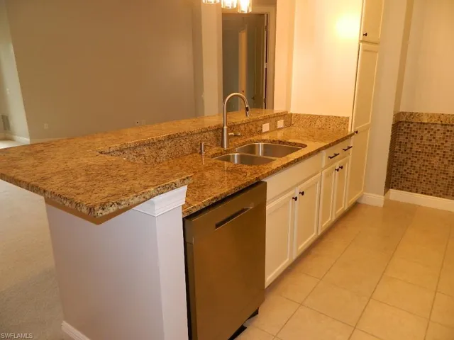 Kitchen with appliances with stainless steel finishes, light stone counters, light tile patterned flooring, white cabinets, and a wainscoted wall