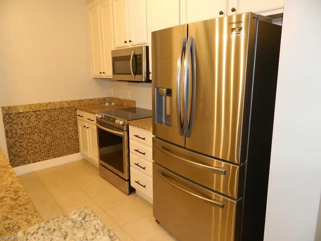 Kitchen featuring appliances with stainless steel finishes, light stone counters, light tile patterned flooring, white cabinetry, and a wainscoted wall