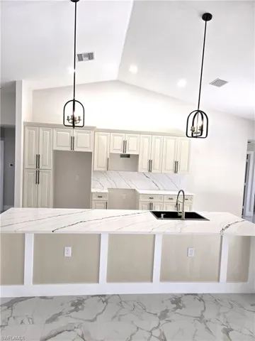 Kitchen with hanging lights, light stone countertops, a spacious island, and vaulted ceiling