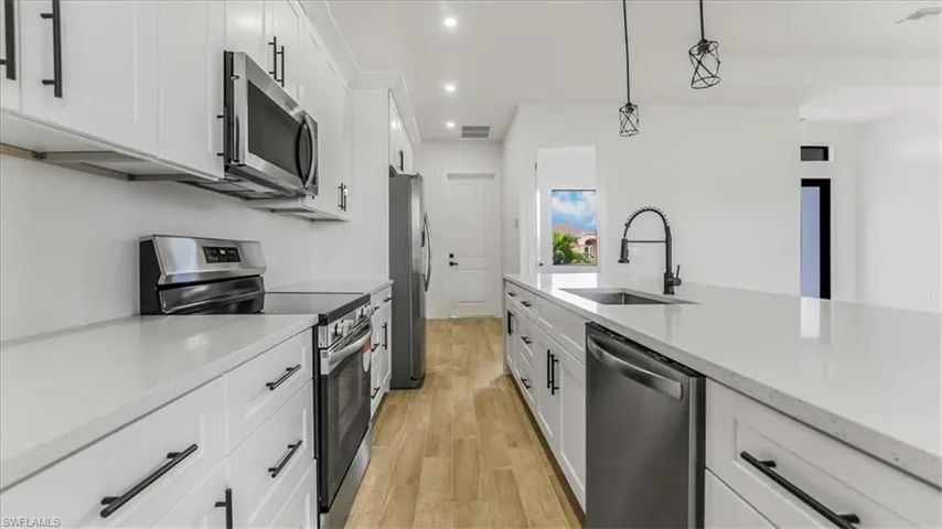 Kitchen featuring appliances with stainless steel finishes, white cabinets, light wood-type flooring, recessed lighting, and light stone countertops