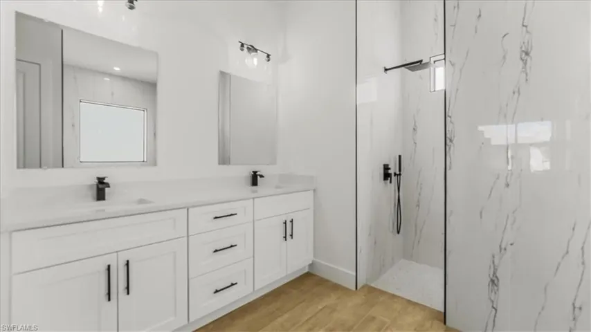 Full bath featuring a marble finish shower, double vanity, and light wood finished floors