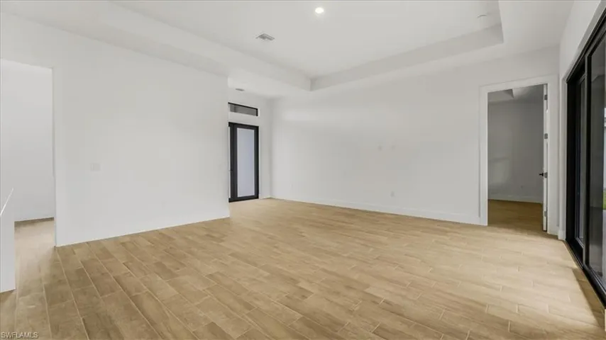 Empty room with a raised ceiling, light wood-style floors, and recessed lighting