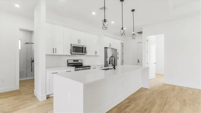 Kitchen with appliances with stainless steel finishes, white cabinetry, light wood finished floors, pendant lighting, and a kitchen island with sink