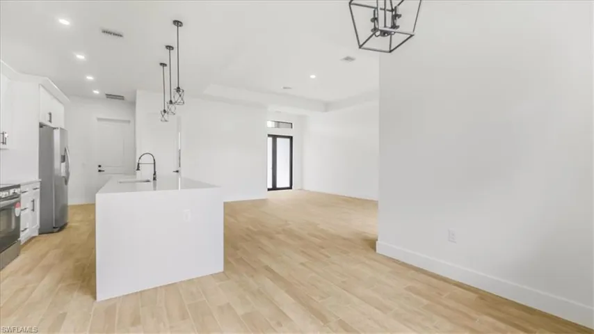 Kitchen with decorative light fixtures, white cabinetry, appliances with stainless steel finishes, a kitchen island with sink, and light wood-type flooring