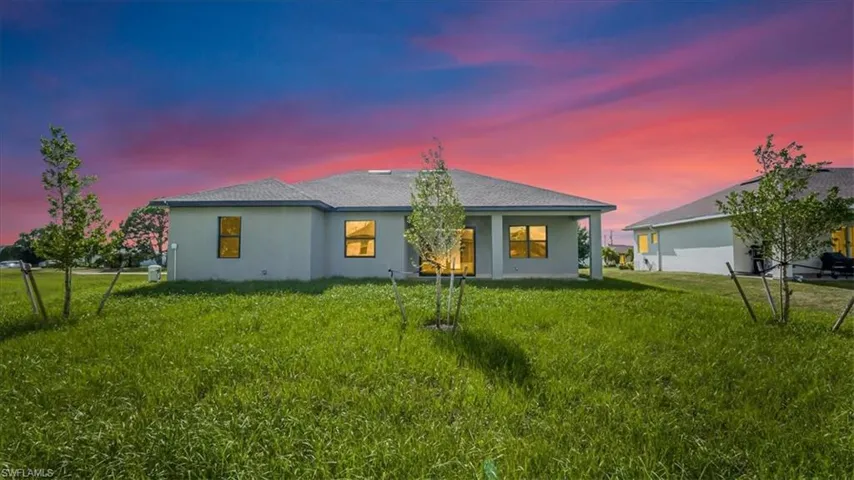 Back of house at dusk featuring a patio, stucco siding, and a shingled roof