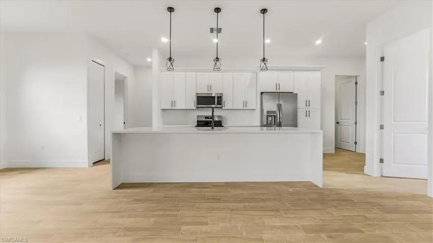 Kitchen with white cabinets, appliances with stainless steel finishes, light wood-type flooring, a large island, and recessed lighting