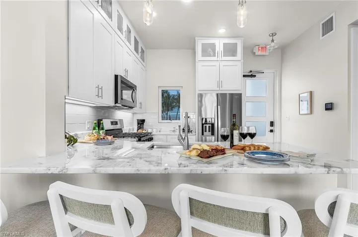 Kitchen featuring white shaker cabinetry, stainless steel appliances, a white subway tile backsplash, and a large island with a light-toned, veined countertop - Virtually Edited Image