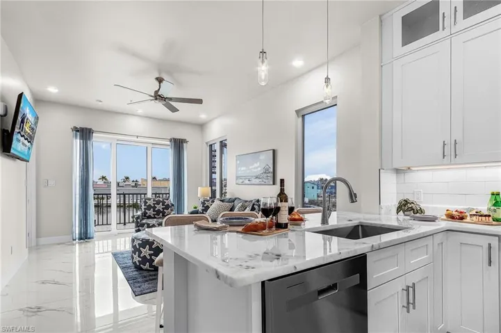 Contemporary kitchen featuring white cabinetry, stone countertops, a stainless steel sink, and an integrated dishwasher - Virtually Edited Image