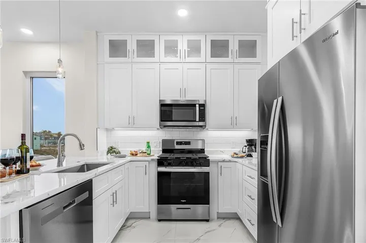 Modern kitchen featuring white shaker cabinetry, stainless steel appliances, marble-look countertops, a subway tile backsplash, and recessed lighting - Virtually Edited Image