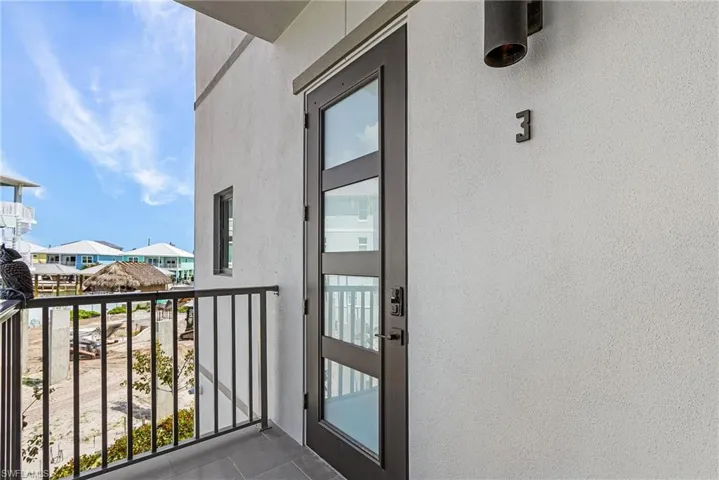 Contemporary entry door with frosted glass panels and sleek black hardware, opening onto a private balcony with black metal railings - Virtually Edited Image