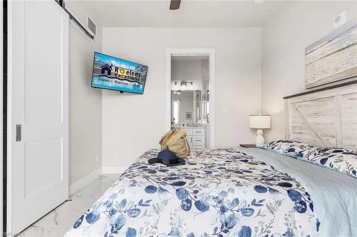 Bright room featuring white barn door, marble-look tile flooring, and a wall-mounted television - Virtually Edited Image