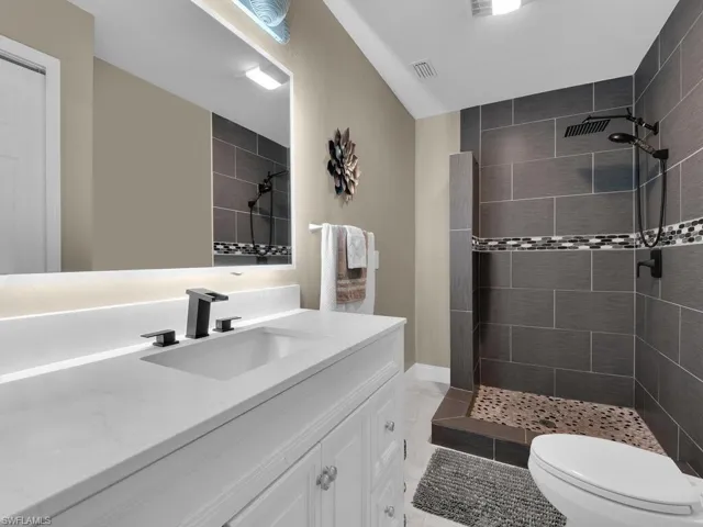 Bathroom featuring toilet, vanity, tiled shower, and tile patterned flooring