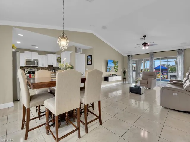 Tiled dining space featuring ceiling fan with notable chandelier, ornamental molding, and lofted ceiling