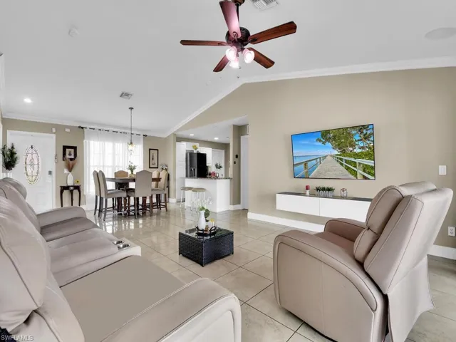 Living room with crown molding, light tile patterned flooring, ceiling fan, and lofted ceiling