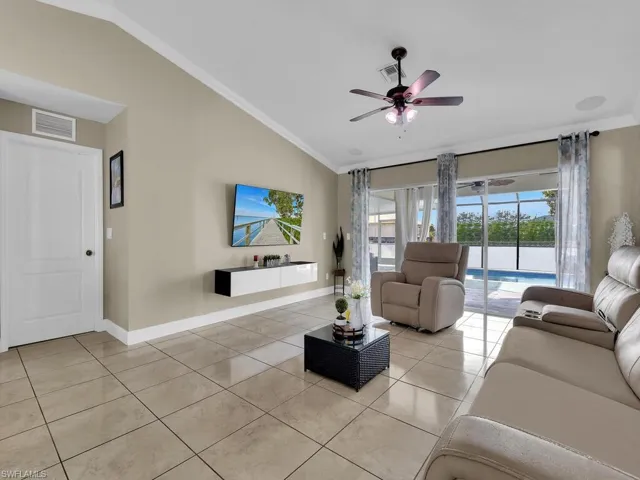Living room featuring ceiling fan, crown molding, light tile patterned floors, and lofted ceiling