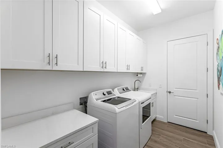 Clothes washing area featuring storage cabinets, wood-type flooring, hookup for a washing machine, washer and dryer, and sink plus storage closet.