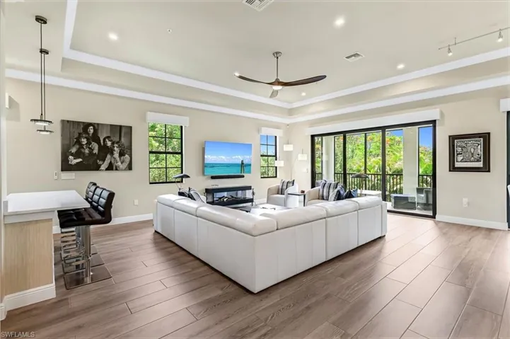 Living room with rail lighting, ceiling fan, a tray ceiling, and wood-type flooring
