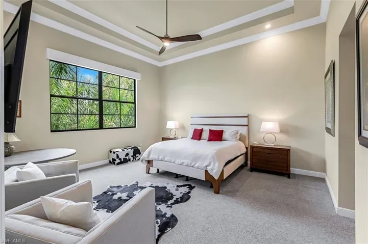 Primary BR w/carpeted bedroom featuring a tray ceiling, ornamental molding, ceiling fan, lutron lighting & shades.