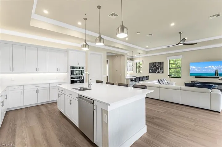 Kitchen with white cabinets, dishwasher, a center island with sink, and a raised ceiling