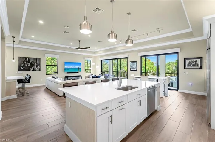 Kitchen with hanging light fixtures, an island with sink, a tray ceiling, white cabinets, and sink