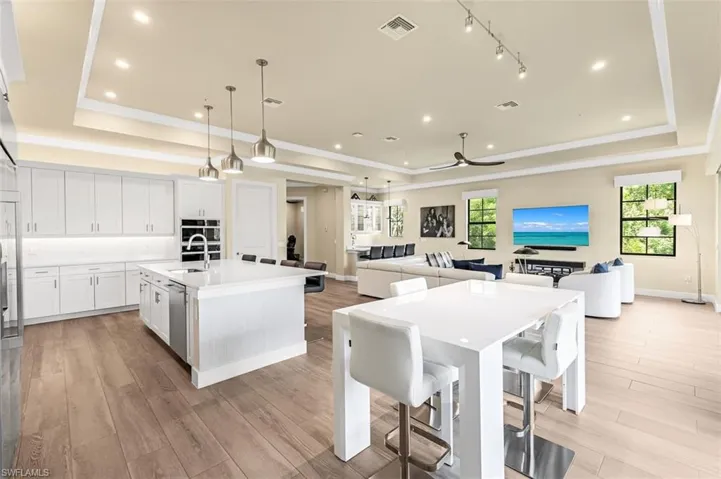 Kitchen featuring a center island with sink, a tray ceiling, decorative light fixtures, and white cabinetry