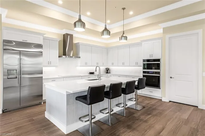 Kitchen with wall chimney range hood, dark hardwood / wood-style flooring, a tray ceiling, built in refrigerator, and sink