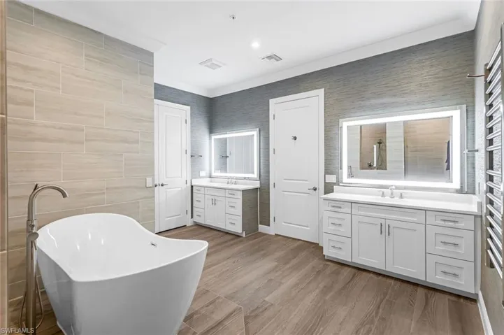 Primary BR with dual LED vanities, wood look porcelain tile and a bathing tub.
