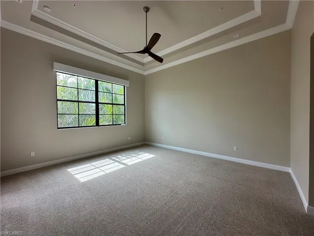 Carpeted empty room featuring ceiling fan, a raised ceiling, and crown molding