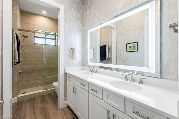 Bathroom with an enclosed shower, double sink vanity, hardwood / wood-style flooring, and toilet