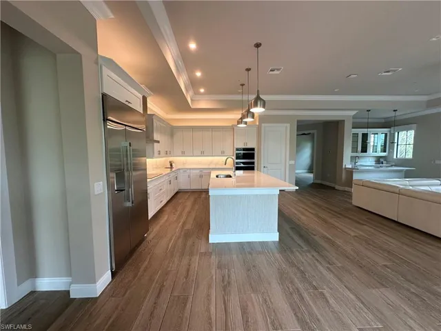 Kitchen featuring stainless steel built in fridge, a kitchen island with sink, hardwood / wood-style floors, sink, and white cabinetry