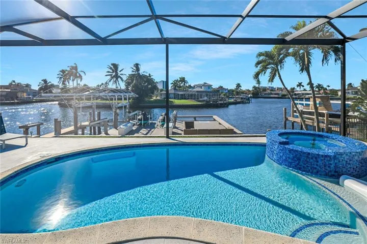 View of swimming pool with a water view, boat lift, a pool with connected hot tub, a boat dock, and glass enclosure