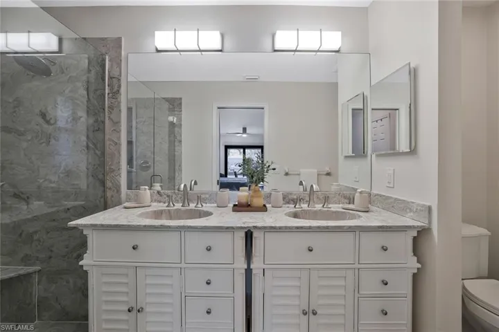 Bathroom with double vanity, a marble finish shower, and a ceiling fan