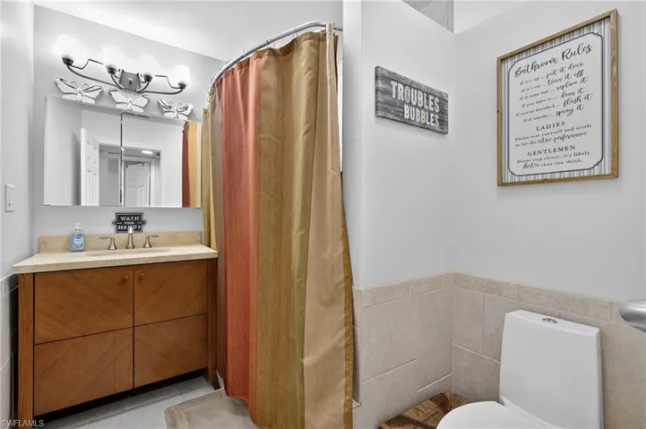 Full bathroom with vanity, wainscoting, tile walls, tile patterned flooring, and curtained shower