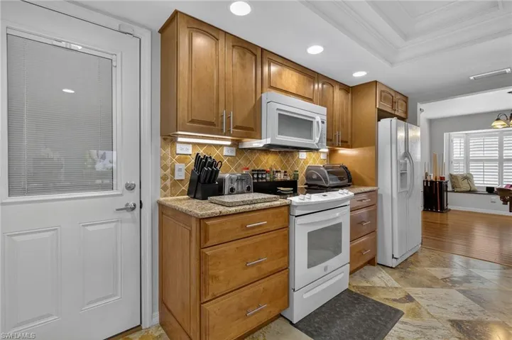 Kitchen with white appliances, crown molding, tasteful backsplash, recessed lighting, and brown cabinets