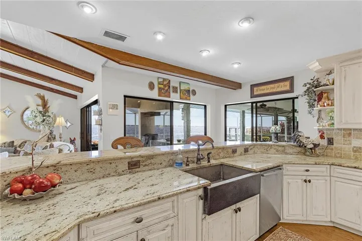 Kitchen with stainless steel dishwasher, open shelves, visible vents, granite countertops, and a copper farmers sink and huge breakfast bar