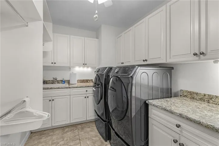 Clothes washing area with washer and clothes dryer, a sink, and cabinet space and granite counters
