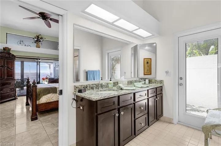 Primary ensuite Bathroom  downstairs featuring tile patterned flooring, double vanity, and exterior door to atrium and south side yard