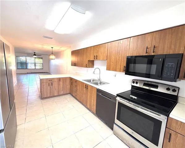 Kitchen with stainless steel appliances, light countertops, wood finish cabinetry, light tile patterned floors, and a peninsula