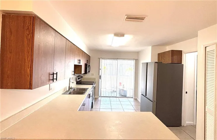 Kitchen with stainless steel appliances, light countertops, light tile patterned floors, a peninsula, and wood finish cabinets