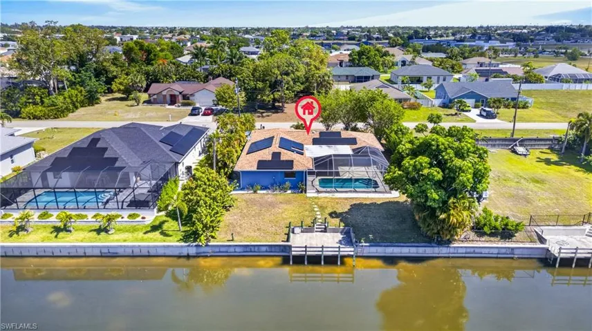 Waterfront property with a private dock featuring a screened-in pool, solar panels, and a manicured lawn